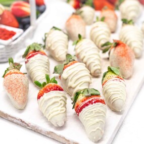 Strawberries Covered In White Chocolate on a white wooden board.