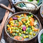 A bowl of soup with carrots, peas and other vegetables.