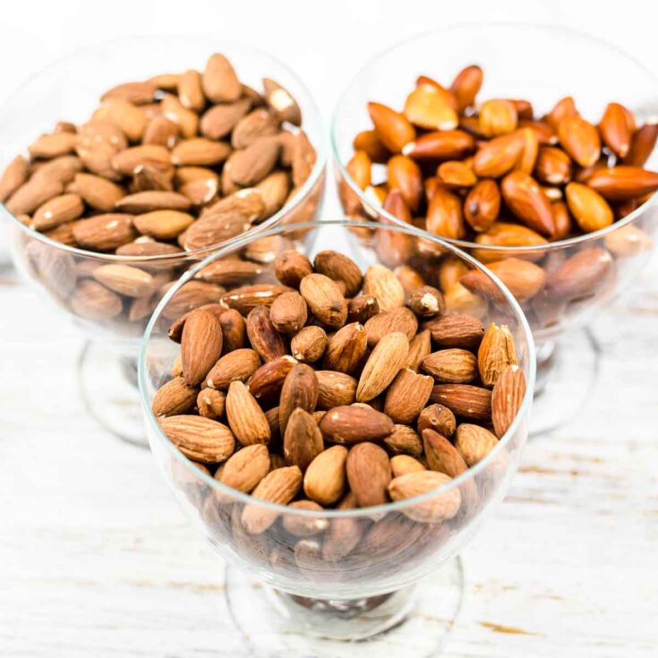 Three bowls of almonds on a wooden table.