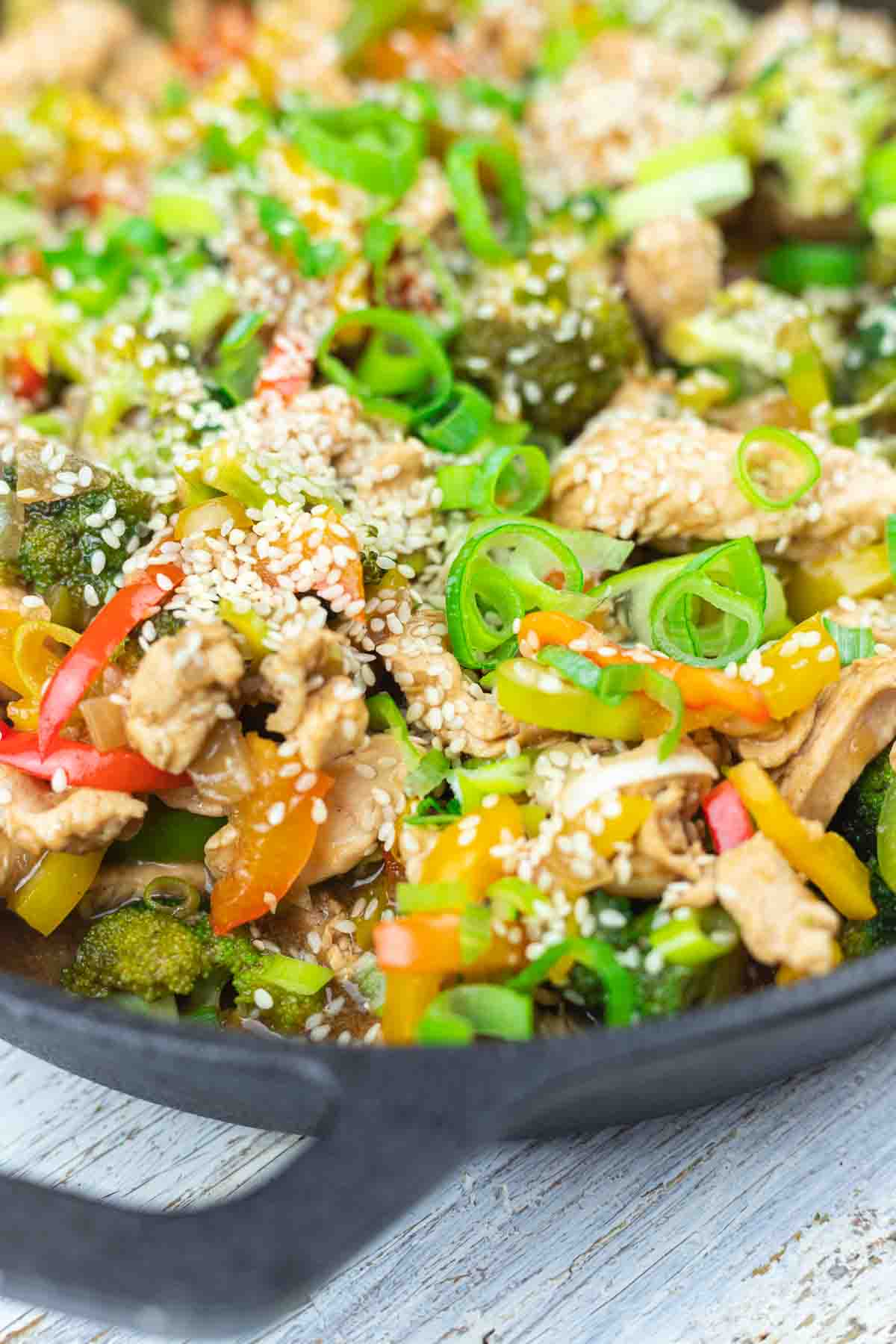 Chicken stir fry in a skillet with vegetables and sesame seeds.