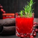 A glass of cranberry drink with rosemary sprigs.