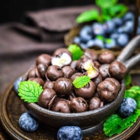 Chocolate covered blueberries in a bowl with mint leaves.