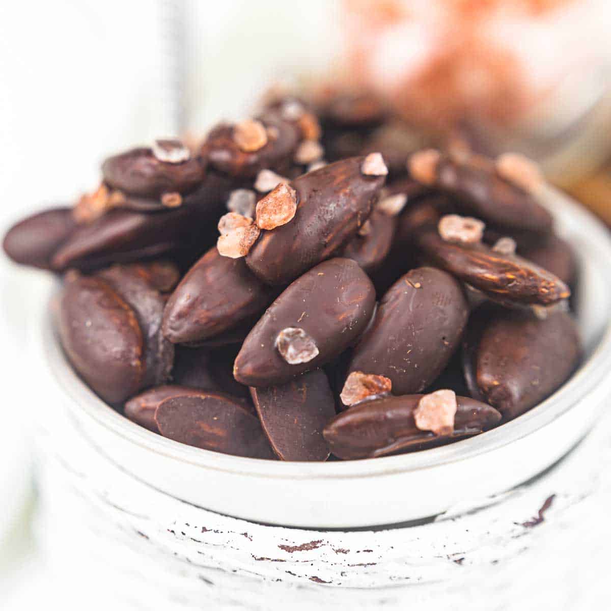 Chocolate covered almonds in a white bowl.
