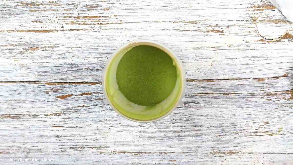 A bowl of green stevia sitting on a wooden table.