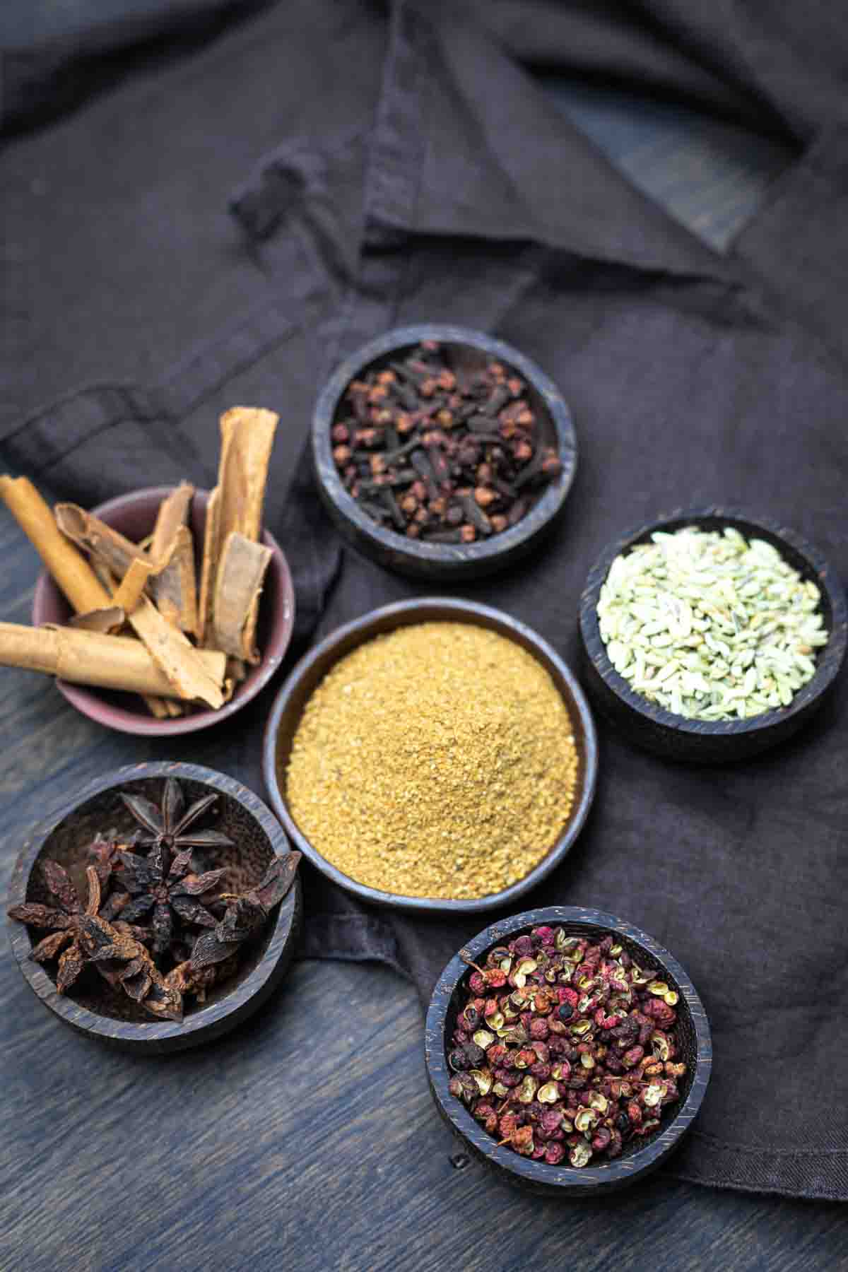 A selection of spices and ingredients in small bowls arranged on a dark wooden surface.