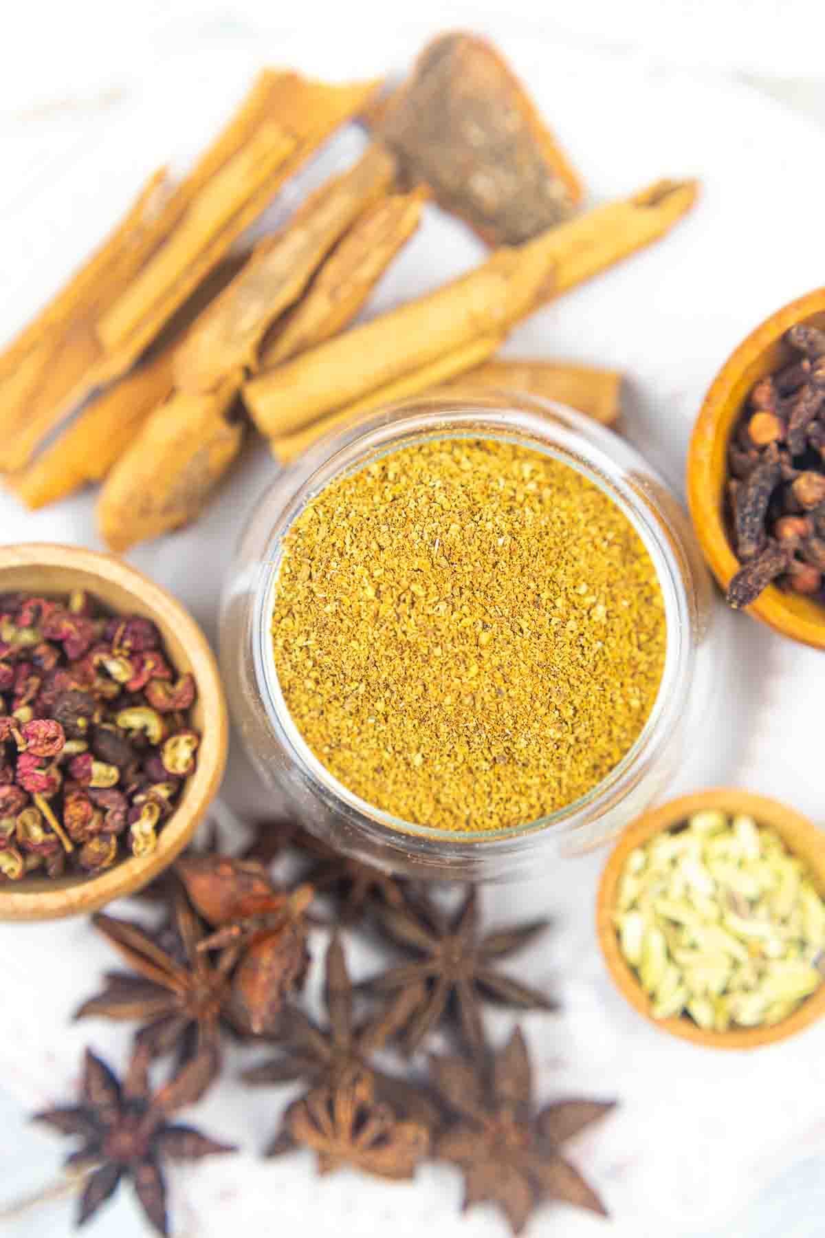 Glass jar of ground spices surrounded by whole spices like cinnamon sticks, cloves, and star anise.