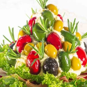 A decorative salad arrangement with green, red, and yellow stuffed peppers, black olives, and sprigs of rosemary, set on a bed of lettuce leaves.