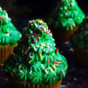Four cupcakes decorated with green frosting and colorful sprinkles to resemble Christmas trees.