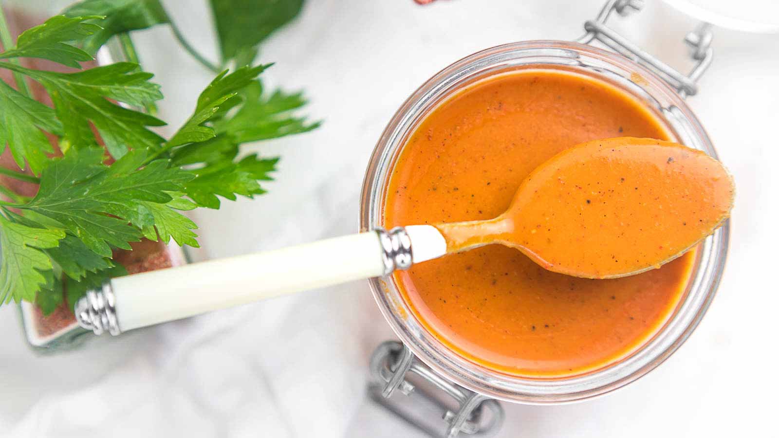 Enchilada Sauce in a glass container with a spoon on top filled with sauce.