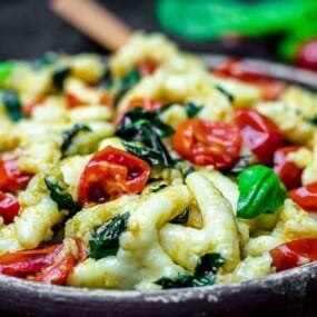 A bowl filled with a mix of gnocchi, cherry tomatoes, and spinach.
