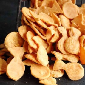 An overturned metal basket spilling out golden, fish-shaped crackers onto a dark surface.