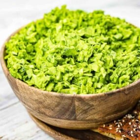 A wooden bowl filled with green vegetable dip is next to a plate of seasoned crackers.