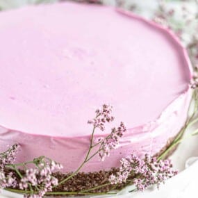 A round pink cake with a crumbly base, surrounded by light pink flowers.