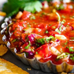 Close-up of a bowl of vibrant salsa with chopped vegetables and herbs, served with triangular pieces of crispy tortilla chips.