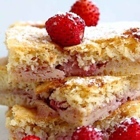 Close-up of three stacked slices of strawberry cake, garnished with whole strawberries and a dusting of powdered sugar.