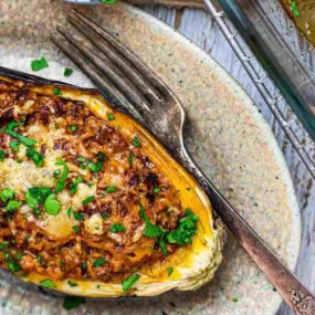 A baked stuffed eggplant topped with melted cheese and garnished with chopped herbs, placed on a plate with a fork beside it.
