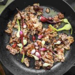 A frying pan with slices of cooked bacon and fresh green onions.