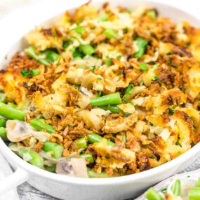 A close-up of a baked casserole in a white dish, containing green beans, mushrooms, crispy fried onions, and a breadcrumb topping.