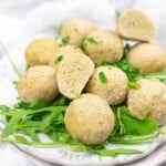 A plate of round dumplings garnished with fresh herbs and served on a bed of arugula.