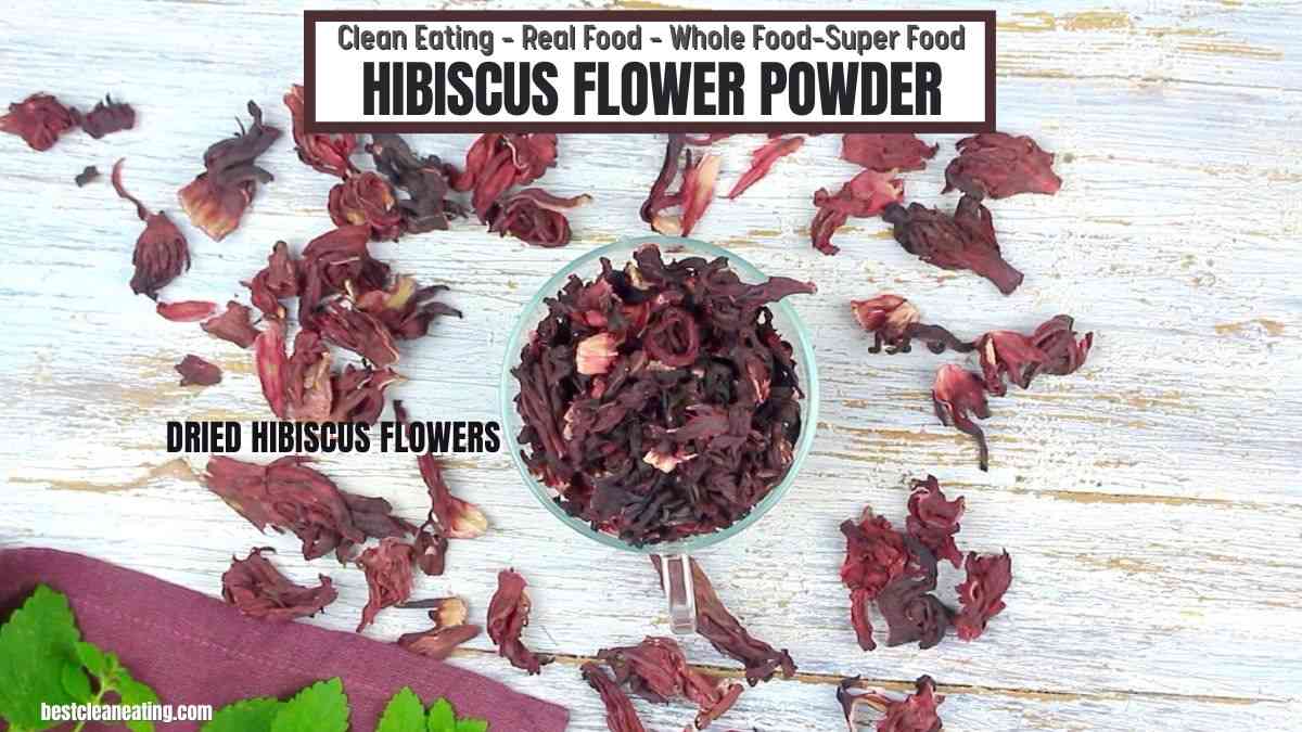 Dried hibiscus flowers scattered around a bowl on a white surface, labeled "HIBISCUS FLOWER POWDER" at the top.