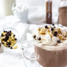 A glass mug of hot chocolate topped with whipped cream, mini marshmallows, and chocolate chips.