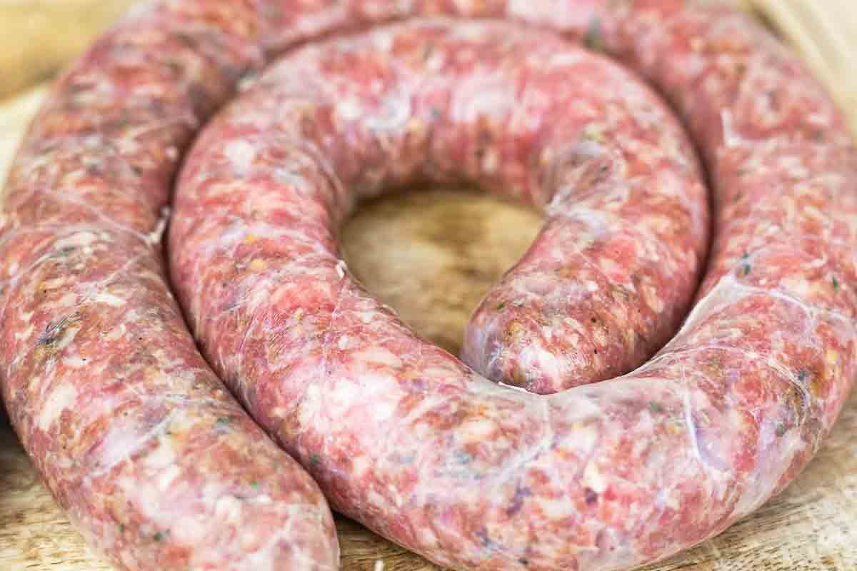 A close-up of raw, coiled sausage on a wooden surface.
