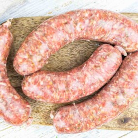 Four uncooked sausages are arranged on a wooden board.