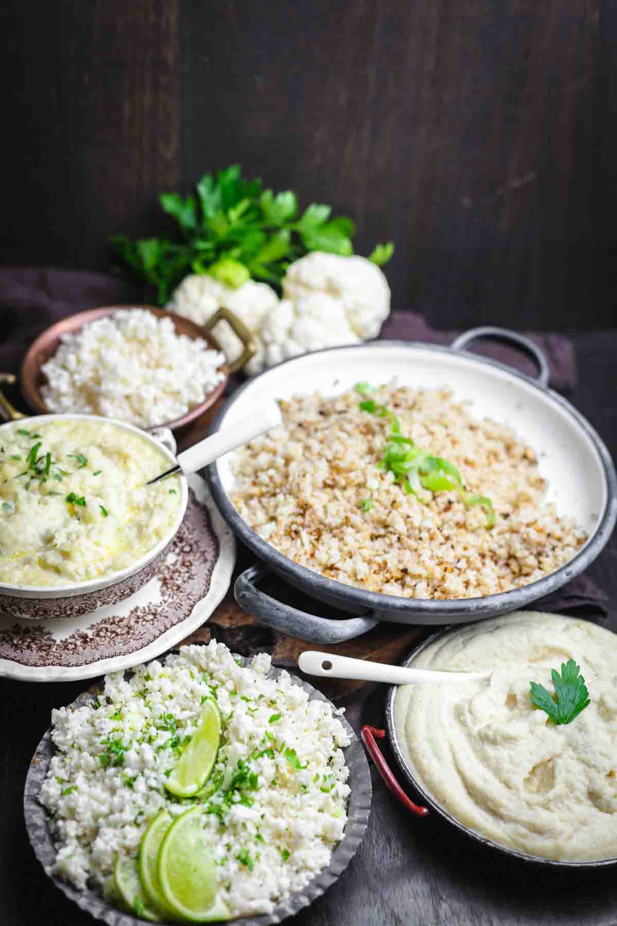 A display of various cauliflower rice dishes with garnishes, set on a dark surface.