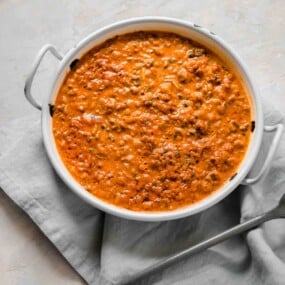 White dish filled with creamy tomato and meat sauce on a gray napkin.