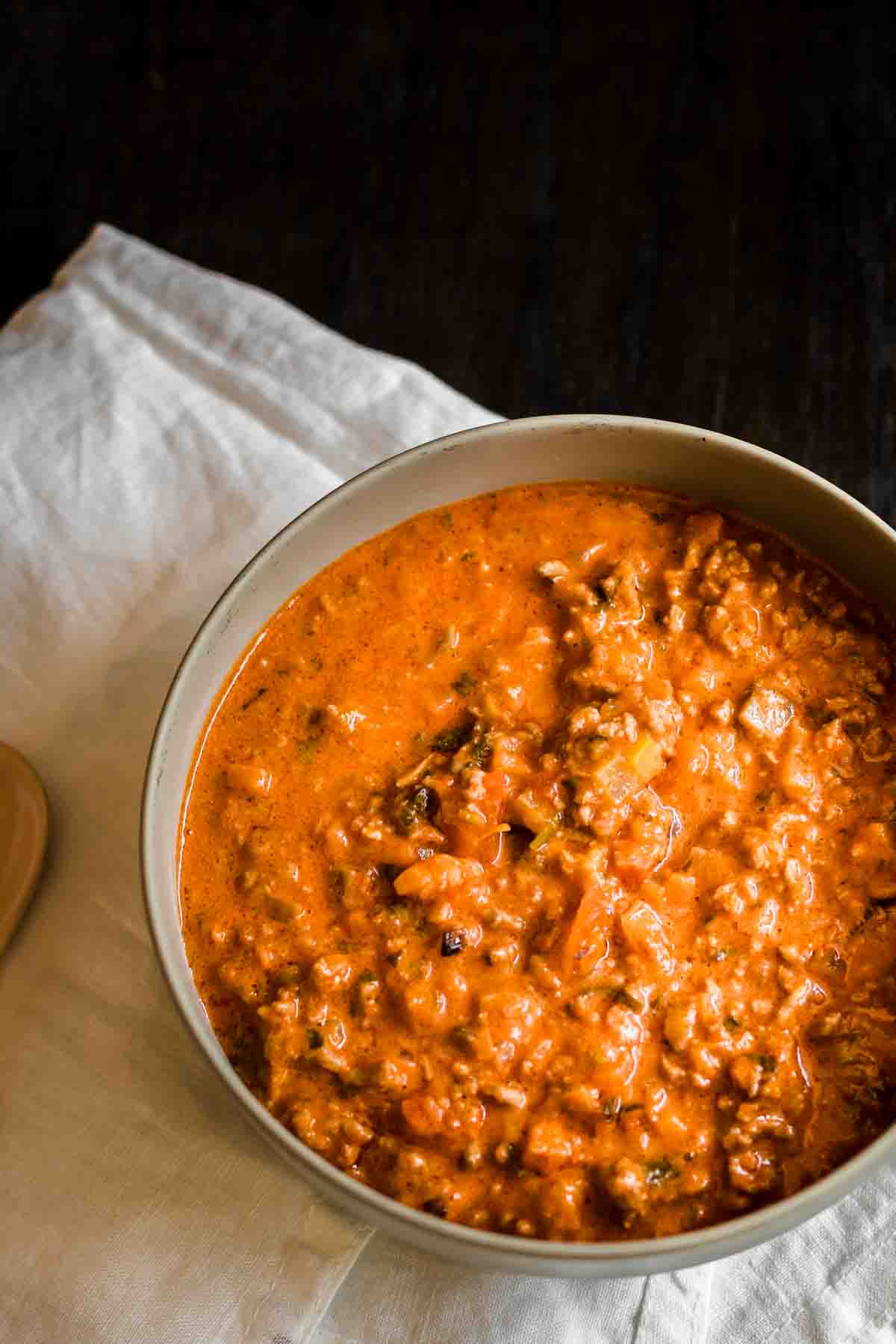 Bowl of red lentil soup with visible chunks on a dark surface and a white cloth napkin beside it.