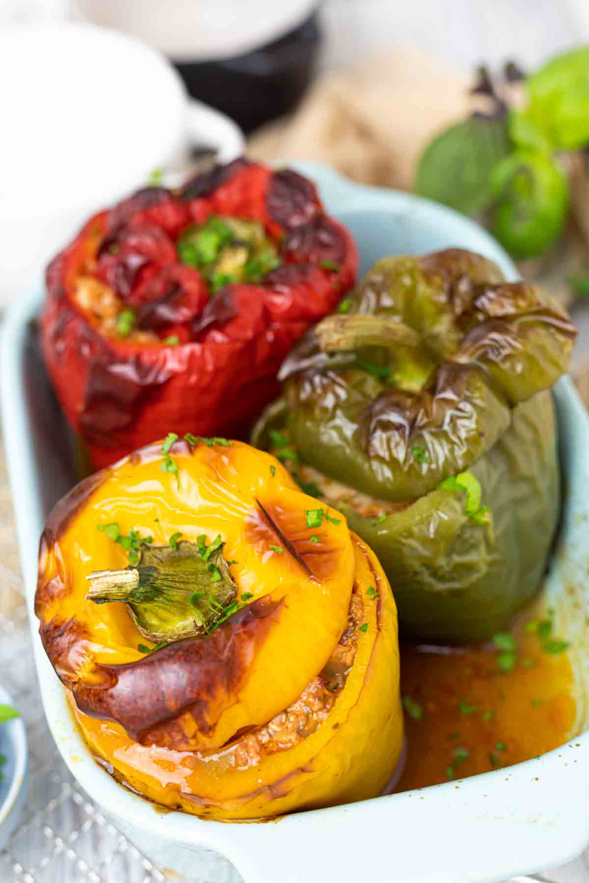Three stuffed bell peppers in red, green, and yellow, baked in a dish, garnished with chopped herbs.