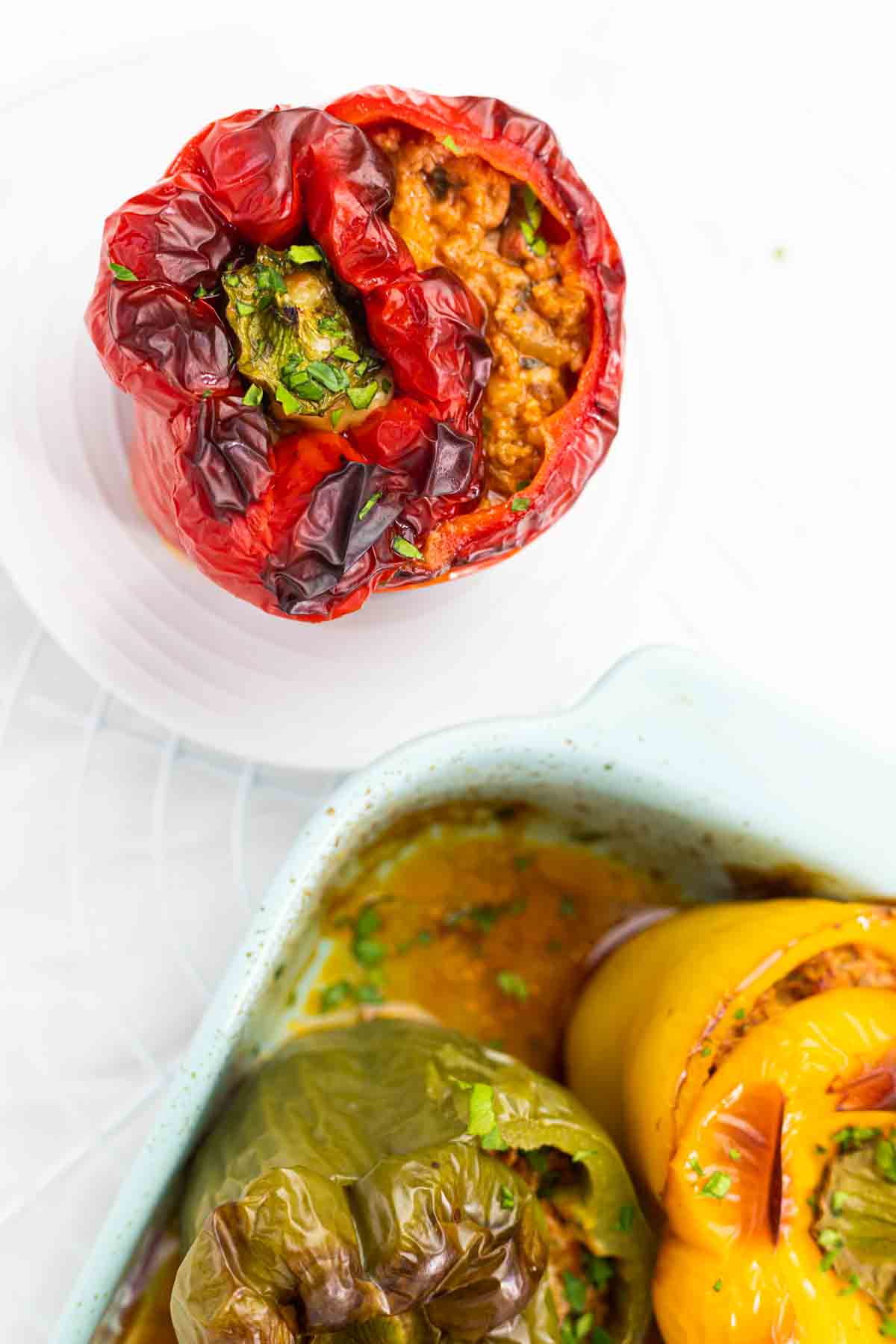 Stuffed red, green, and yellow bell peppers filled with a meat and herb mixture baked in a light-colored dish.