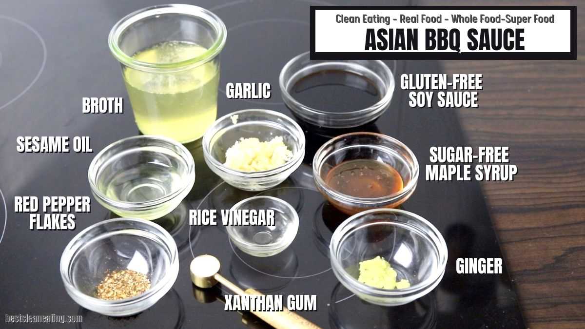 Various ingredients for Asian BBQ Sauce labeled on a stovetop: broth, garlic, gluten-free soy sauce, sesame oil, sugar-free maple syrup, red pepper flakes, rice vinegar, ginger, xanthan gum.