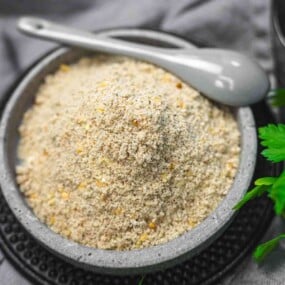 A bowl filled with almond flour and a gray spoon on a black plate, garnished with green leaves.