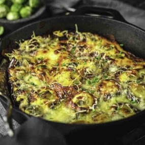 A cast iron skillet with a cheesy, baked dish garnished with herbs, set on a cooling rack.