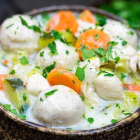 A bowl of creamy soup with chicken, vegetables, and dumplings.