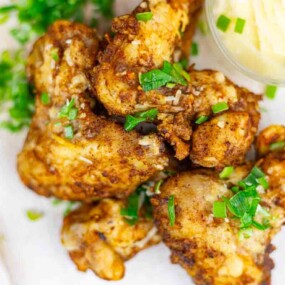 Fried chicken pieces garnished with chopped green herbs, served next to a container with a light-colored dip.