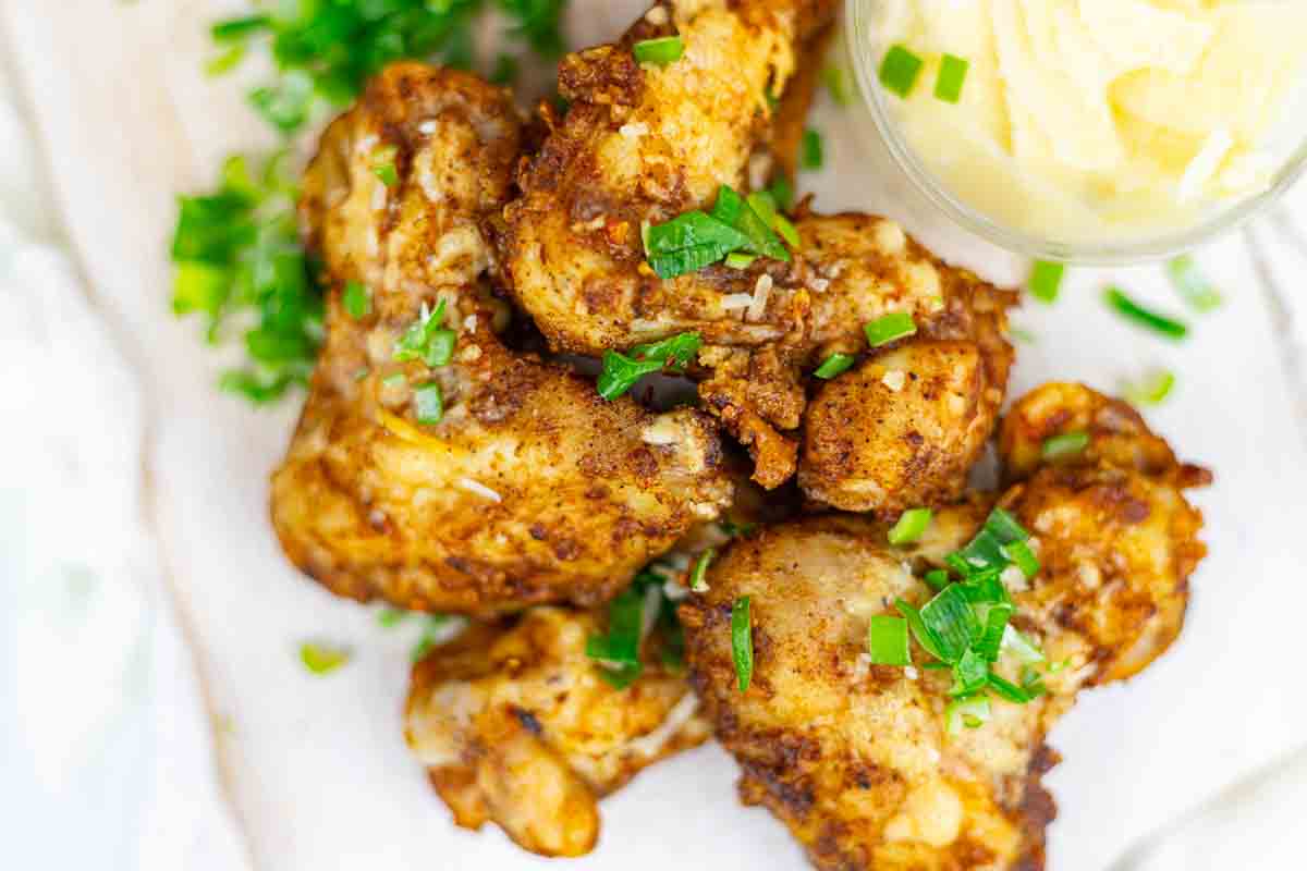 Fried chicken pieces garnished with chopped green herbs, served next to a container with a light-colored dip.