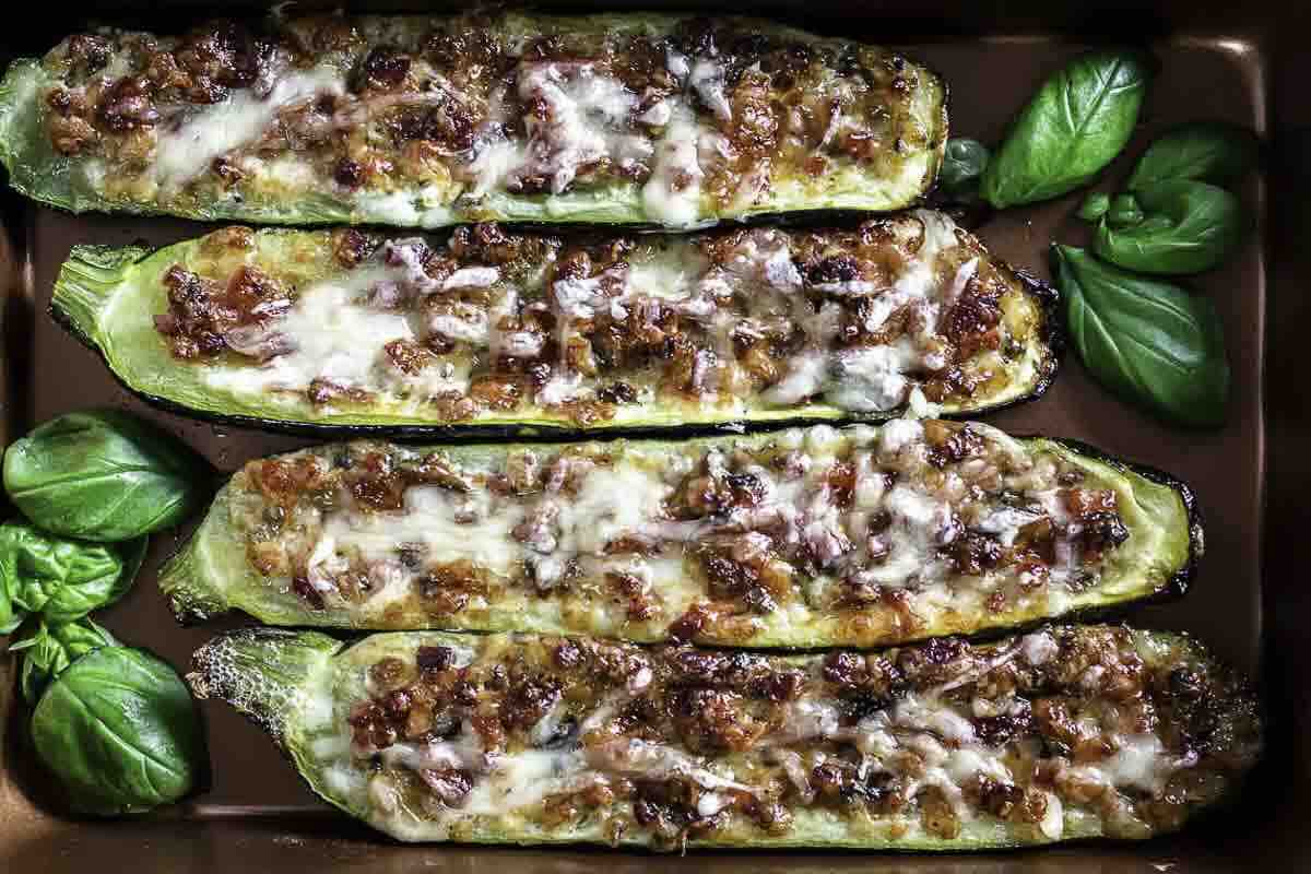 A baking tray with stuffed zucchini boats topped with cheese.