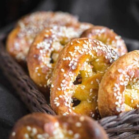 Close-up of a basket containing several soft pretzels topped with sesame seeds, arranged in a row.