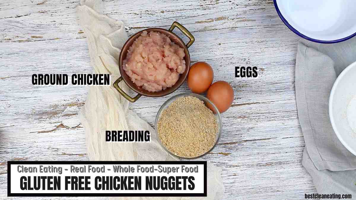 Top-down view of ground chicken in a bowl, two eggs, and a bowl of breading on a light wooden surface; labeled as ingredients for gluten-free chicken nuggets.