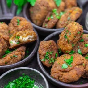 Bowls filled with golden-brown, breaded and fried patties garnished with chopped parsley, with a small bowl of additional parsley nearby.