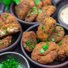 Three bowls filled with golden-brown chicken nuggets garnished with chopped parsley, served with a small bowl of creamy dipping sauce.