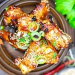 Grilled chicken drumsticks topped with sesame seeds and sliced green onions, served in a brown bowl with leafy greens in the background.