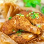 Close-up of two seasoned and baked chicken legs garnished with chopped green onions, placed on brown parchment paper.