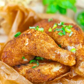 Two pieces of seasoned, breaded fried chicken garnished with chopped green onions on brown parchment paper.