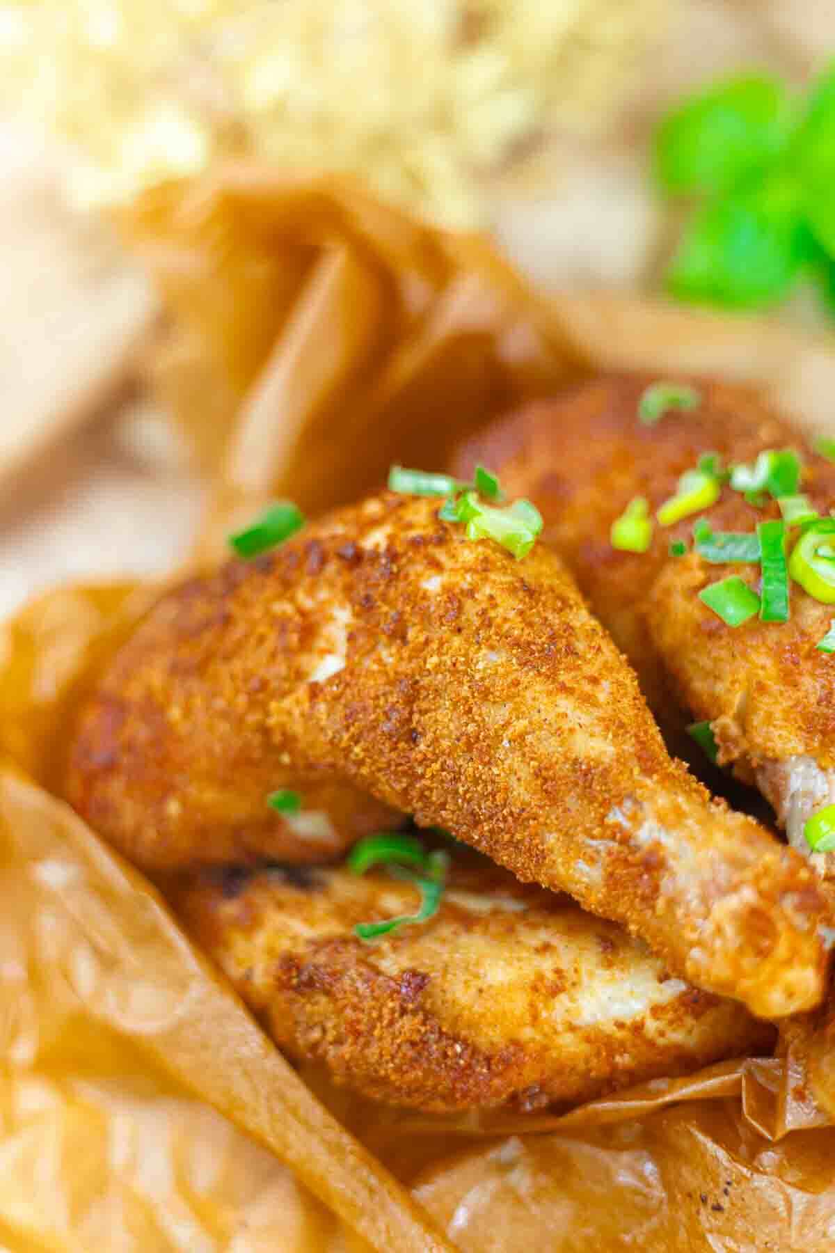 Two pieces of seasoned, baked chicken with a crispy coating, garnished with chopped green onions, served on brown parchment paper.