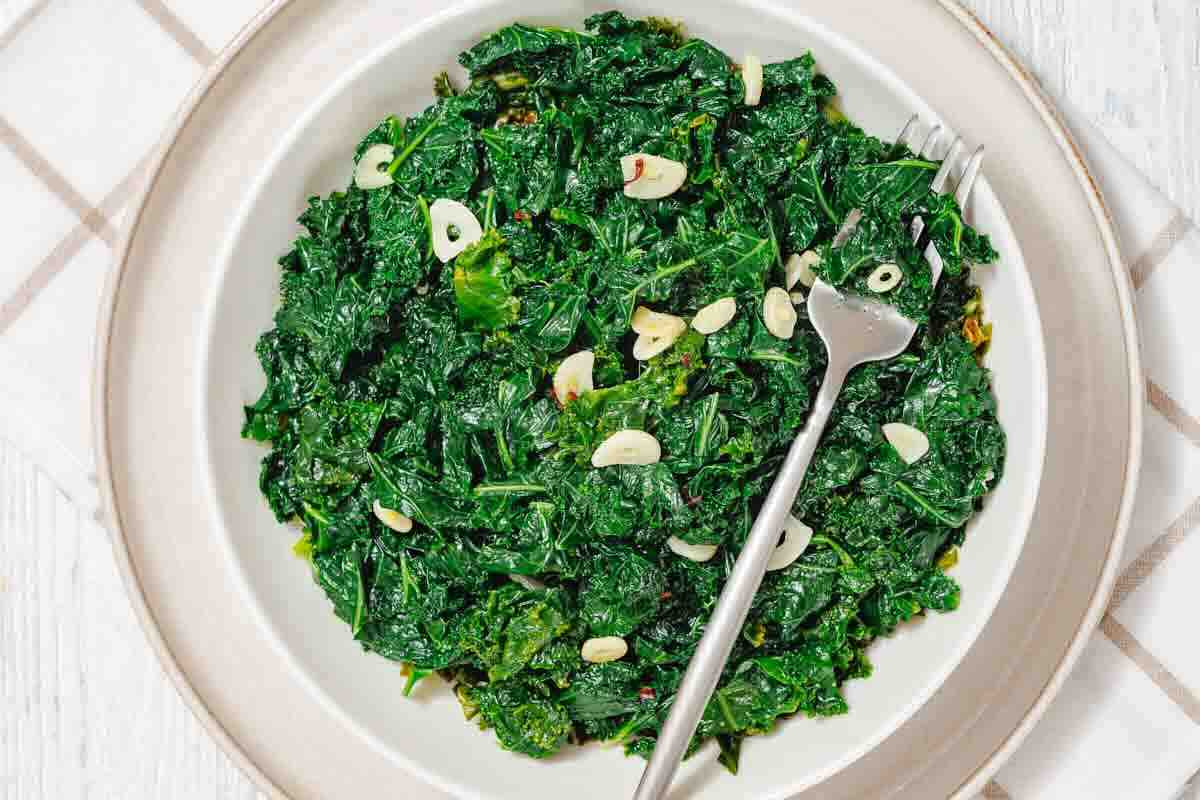 A plate of sautéed kale with sliced garlic, served with a fork on a white plate over a checked cloth.