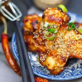 Grilled chicken wings topped with sesame seeds and chopped green onions, served on a blue patterned plate with chopsticks beside them.