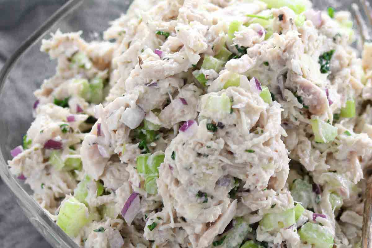 Close-up of chicken salad with chunks of chicken, diced celery, red onion, and herbs mixed with a creamy dressing.